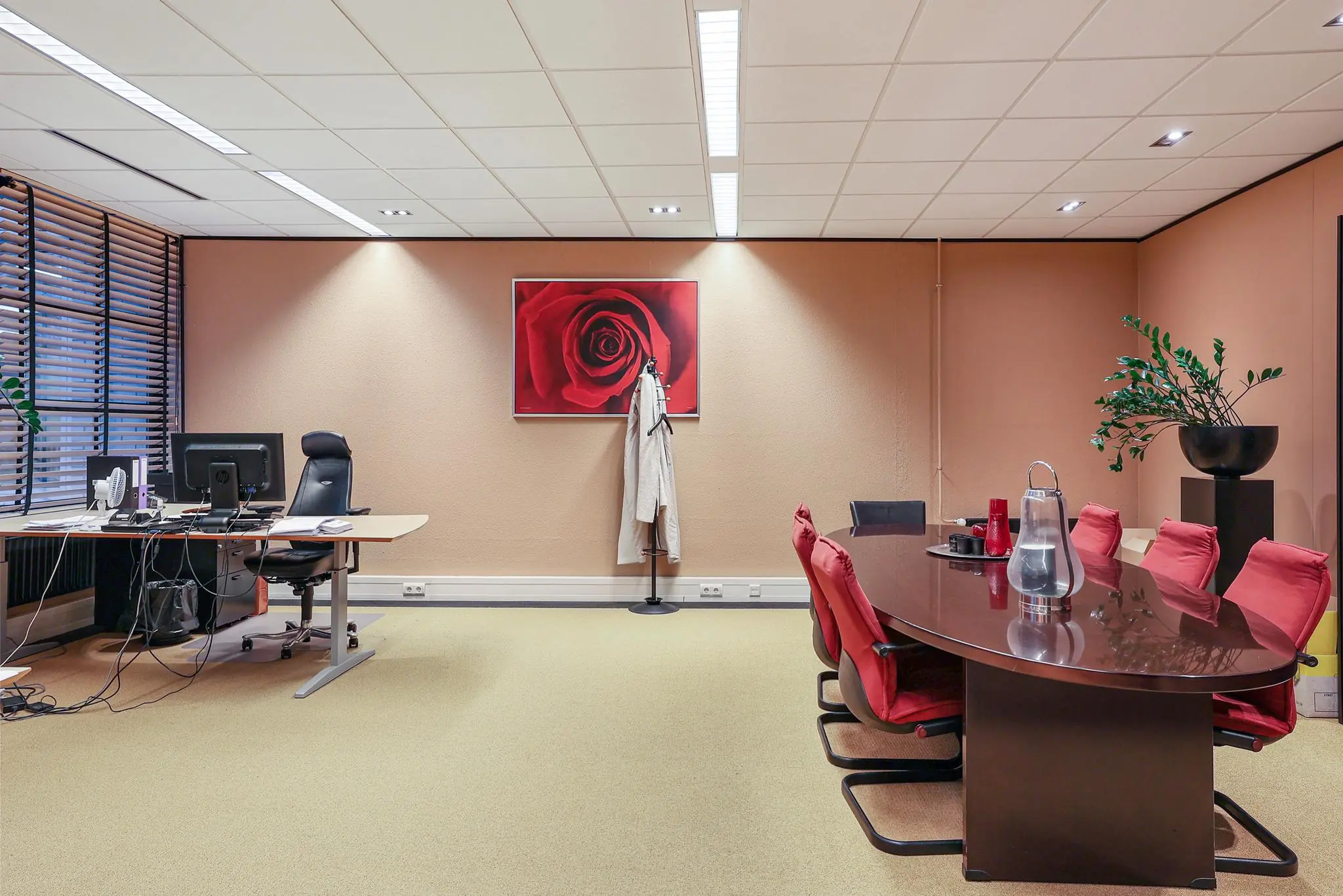 Vergaderruimte met een ovale tafel, rode stoelen, bureau en wanddecoratie aan de Oude Utrechtseweg.